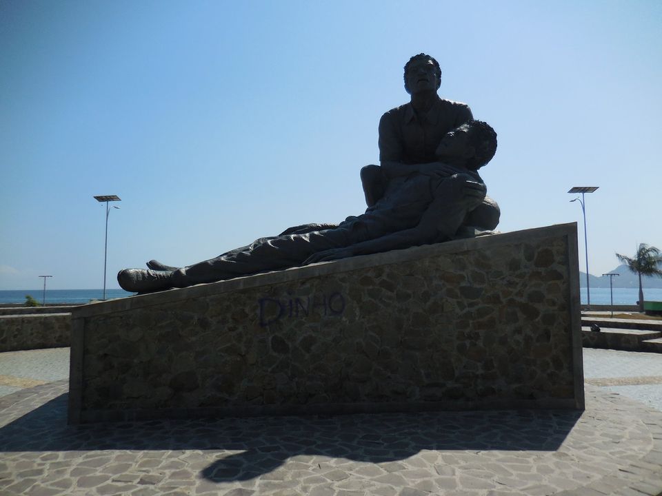 An image of a statue with one man laying on the ground and another man crouchd beside him supporting his head