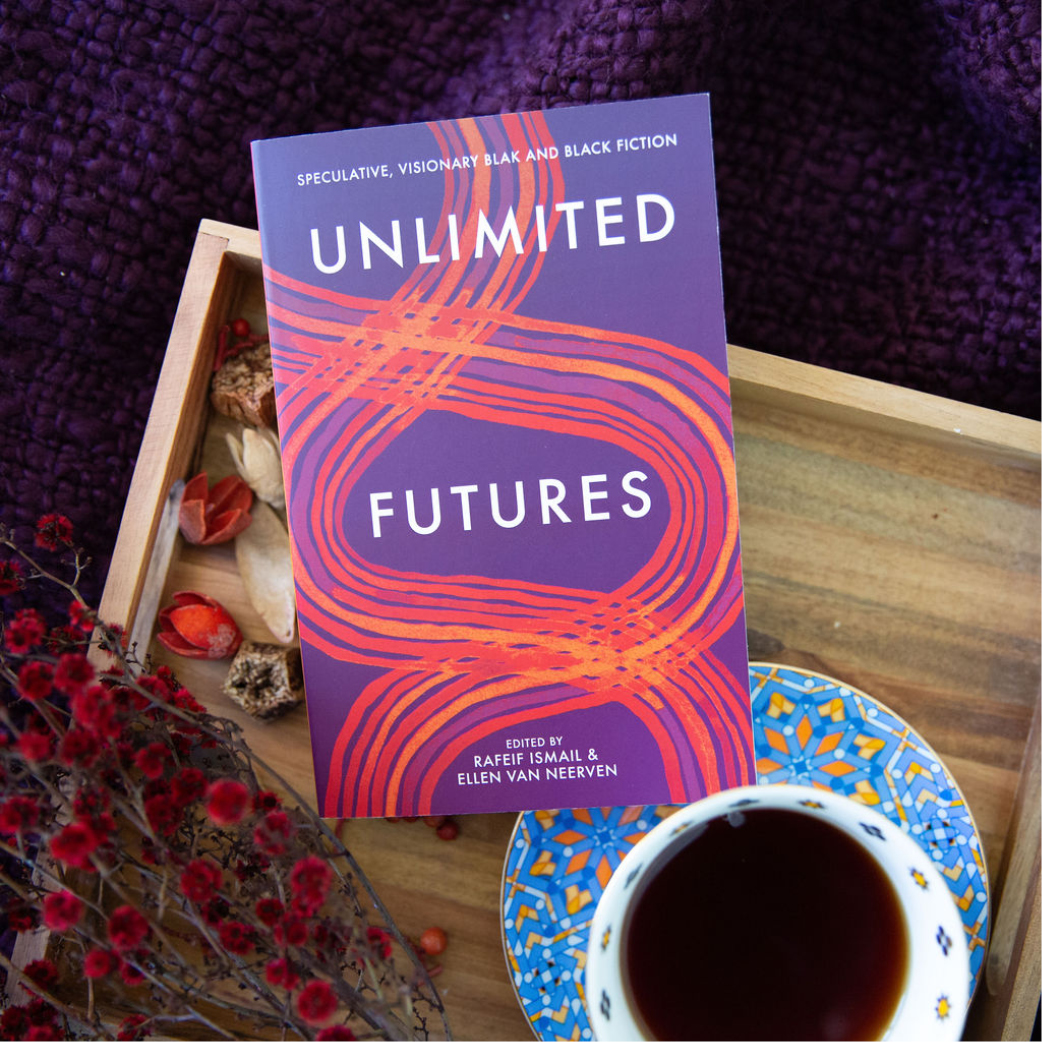 Image of the book, Unlimited Futures, sitting on a wooden tray with a blue teacup and saucer sitting next to the book.